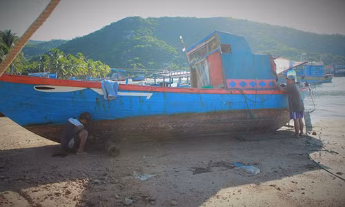 Sáu Thanh và Hai Mạnh tranh thủ cạo xác hà bên mạn thuyền râm mát khi mặt trời dần lên cao. Ảnh: Hoàng Như.