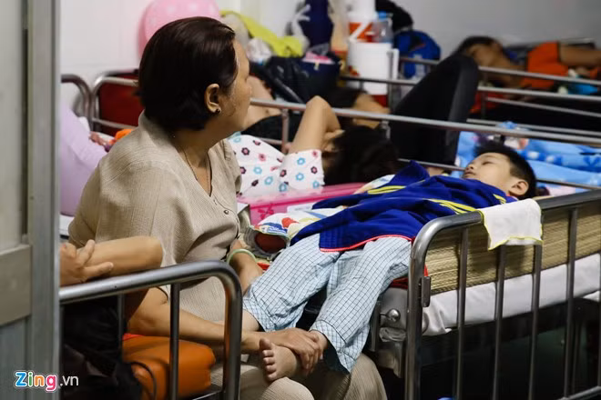 Trong phòng, một giường bệnh có tới 3 bệnh nhi cùng chung, nằm tráo đầu đuôi. Một bé trai phải nằm ngang thò chân xuống cho bà đỡ.