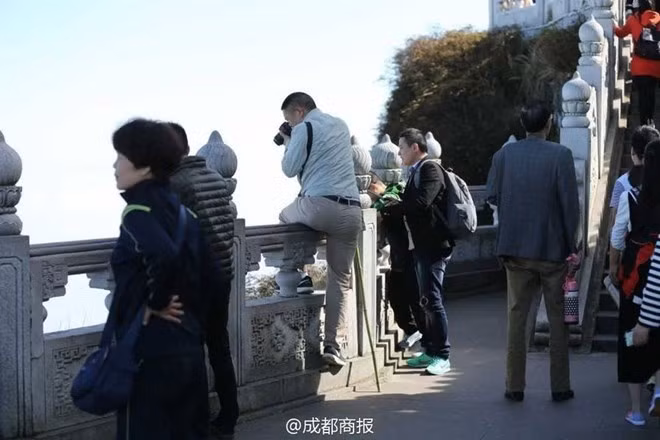 Một du khách Trung Quốc vắt chân qua lan can để cố gắng chụp một bức ảnh phong cảnh đẹp. (Nguồn: QQ News)