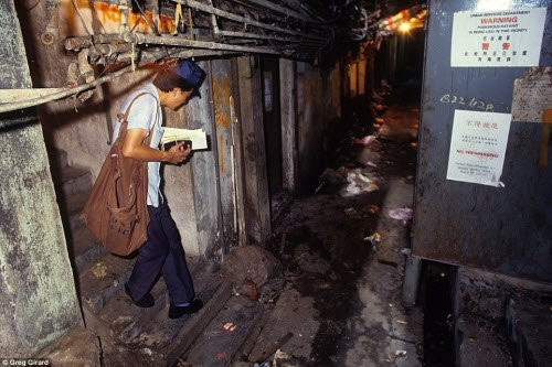 Nhân viên bưu điện mò mẫm dưới lối đi tối tăm với đầy dây cáp tại khu ổ chuột để đưa thư và bưu phẩm cho khách hàng.