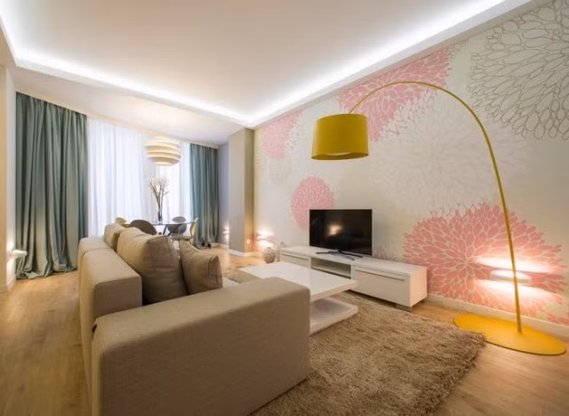 Để tăng thêm độ thoáng sáng cho không gian sống, vợ chồng gia chủ đã chọn lựa bộ sofa với kiểu dáng hiện đại, màu ghi xám đơn giản để tạo tâm điểm cho phòng khách. Bên cạnh đó, sự góp mặt của mảng tường với giấy dán họa tiết dịu dàng từ hồng pastel và màu be đủ để căn phòng trở nên quyến rũ hơn.