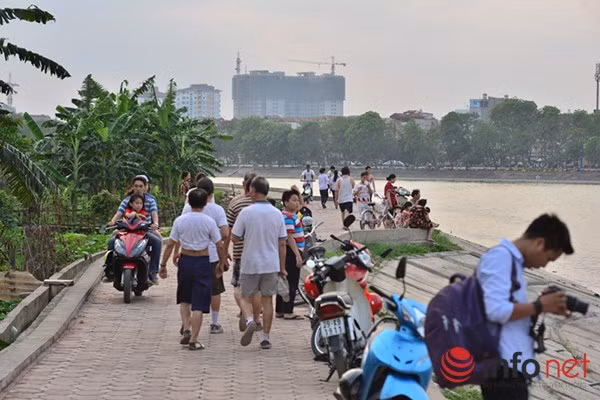 Trên bờ hồ, người qua lại đi bộ tập thể dục, dưới hồ đông nghịt người tắm tránh nóng.