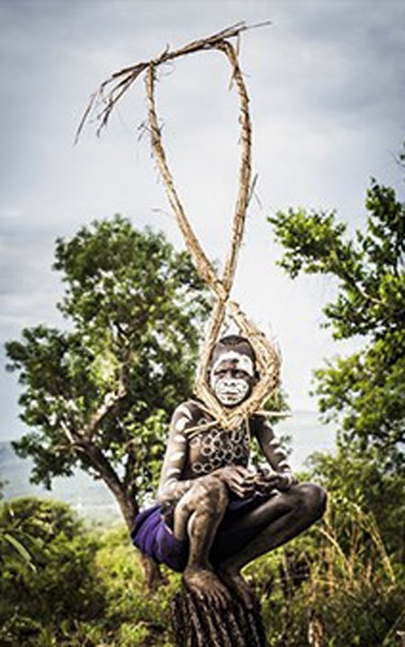 Seton phải mất ba ngày lái xe từ Addis Ababa để đến chụp ảnh bộ lạc Suri, cư trú tại làng Naregeer trong thung lũng Omo Rover - một khu vực xa xôi của Ethiopia, gần biên giới của Nam Sudan. Đây là bức ảnh đầu tiên trong ngày, bấm máy vào lúc 6h00, cậu bé bộ lạc Suri ngồi trên một thân cây khô giữa cánh đồng lúa miến.