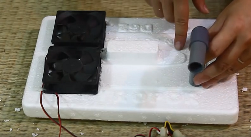 Bước 3: Đặt chiếc quạt điện lên trên tấm thùng xốp vừa cắt, bên còn lại đặt chiếc ống nhựa hình chữ L lên, sau đó dùng keo dán dán chặt lại.