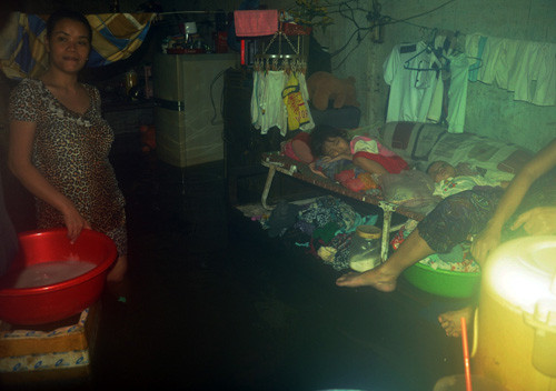 Chị Nhàn giặt đồ trong nước ngập. Bên cạnh chị đứng là chiếc giường xếp nơi hai con nhỏ chị đang say giấc trong “những ngày nước nổi ở Sài Gòn”.