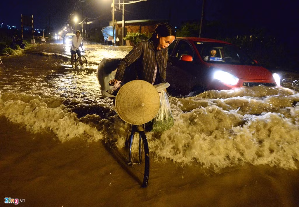 Ôtô đi qua tạo sóng đánh vào những người lao động đang dắt xe đạp qua vùng nước ngập.