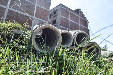 Những đống vật liệu, cột điện... vứt ngổn ngang giữa bãi cỏ mọc um tùm.