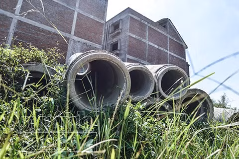 Những đống vật liệu, cột điện... vứt ngổn ngang giữa bãi cỏ mọc um tùm.