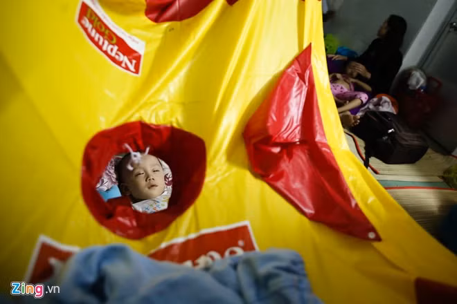 Đêm 6/10, TP HCM có mưa. Chị Phụng, mẹ bé Văn Ngọc Thảo Nhi phải lấy áo mưa để che cho con không bị tạt ướt. Chị cho biết, bé bị viêm phổi nặng, nằm hành lang rất không tốt cho việc chữa trị căn bệnh này.