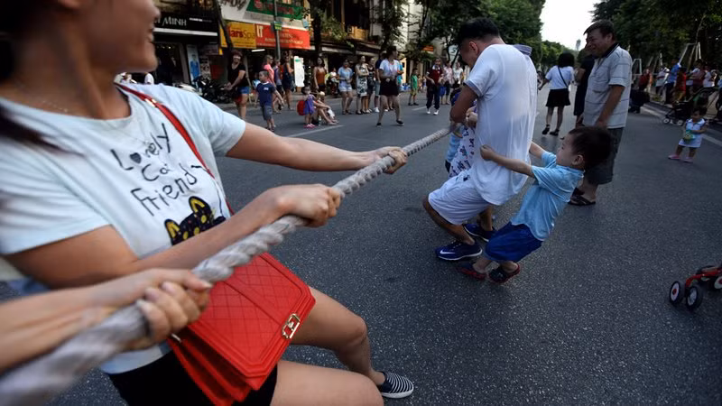 Cậu bé cố giúp sức cha trong trò chơi kéo co diễn ra giữa lòng đường Đinh Tiên Hoàng.