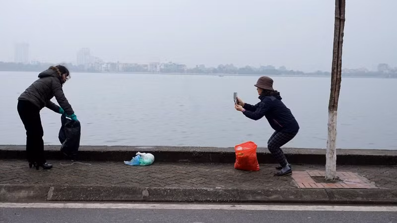 Những phụ nữ tự nguyện dọn rác ven Hồ Tây tranh thủ dùng smartphone lưu giữ hình ảnh tham gia hoạt động công ích.