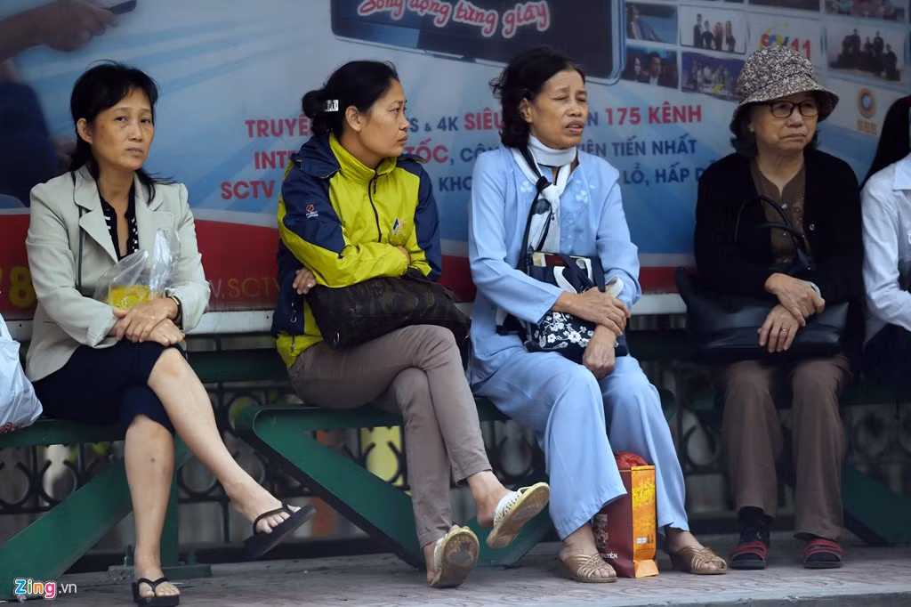 Các bà các cô với áo khoác ấm, khăn quàng ngồi bến xe buýt trên đường Kim Mã.