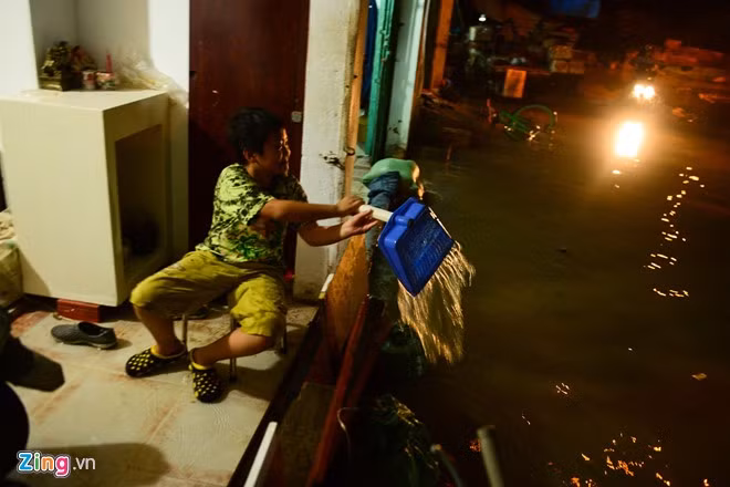 Sau khi nước rút thấp hơn thềm nhà, bé Ngô Hồng Huy ngồi hì hụi tát nước ra ngoài.