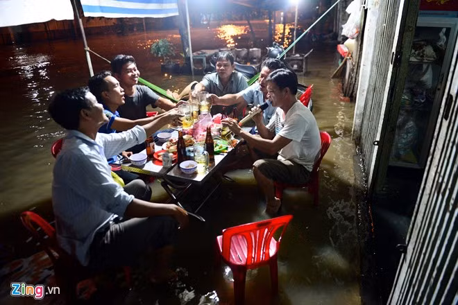 Nhóm đàn ông tụ tập nhậu ngay ngoài vỉa hè, bất chấp dòng nước ngập dưới chân.