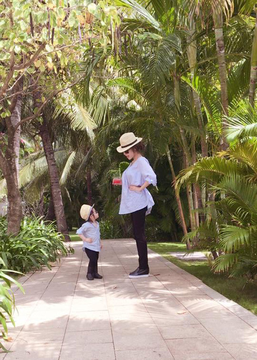 Con gái Elly Trần diện set đồ khá giống mẹ gồm: áo sơ mi màu xanh, quần đen, giày da, mũ và kính mát. 