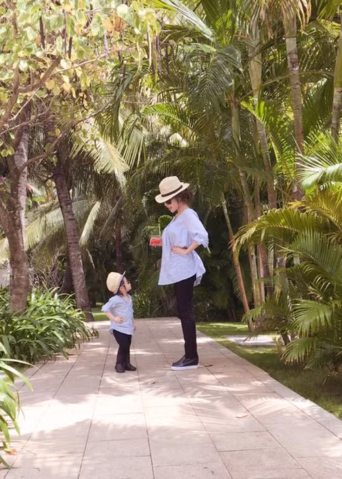 Con gái Elly Trần diện set đồ khá giống mẹ gồm: áo sơ mi màu xanh, quần đen, giày da, mũ và kính mát. 