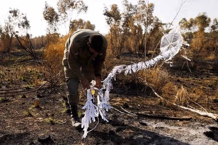 Một người lính Israel đứng bên một con diều cháy dở được thả qua biên giới và rơi vào phần đất Israel.