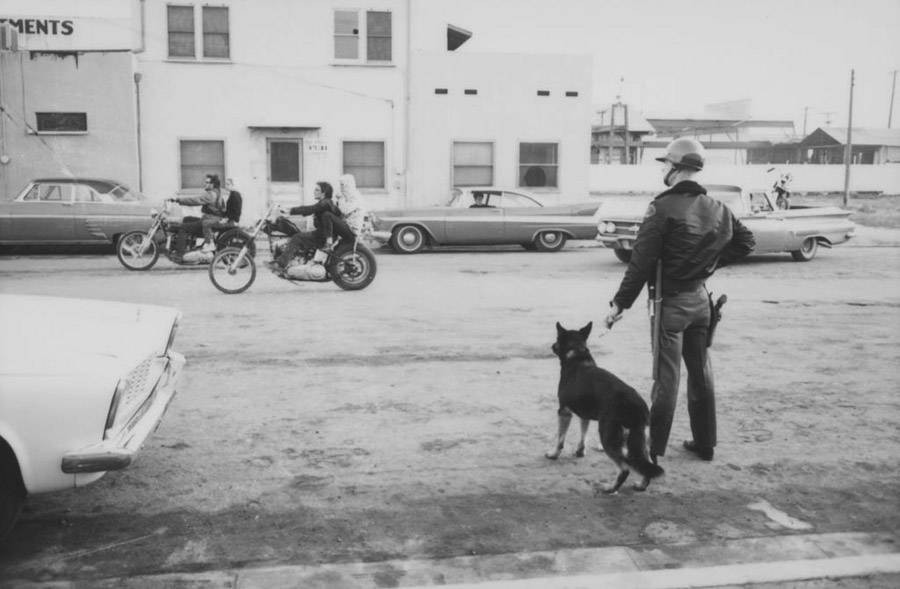 Cảnh sát đứng theo dõi khi xe mô tô của băng đảng Hells Angels đi qua bên ngoài quán cà phê Blackboard ở Bakersfield, California, năm 1965.