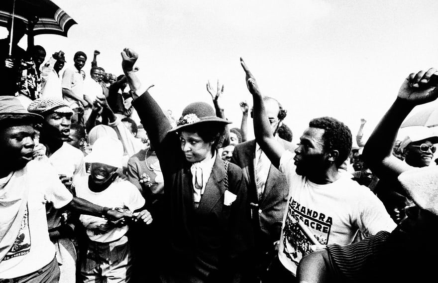 Winnie Mandela giơ tay khi tham dự lễ tang của 17 người da màu thiệt mạng trong một vụ bạo động ở Johannesburg năm 1986. Ảnh: AP.