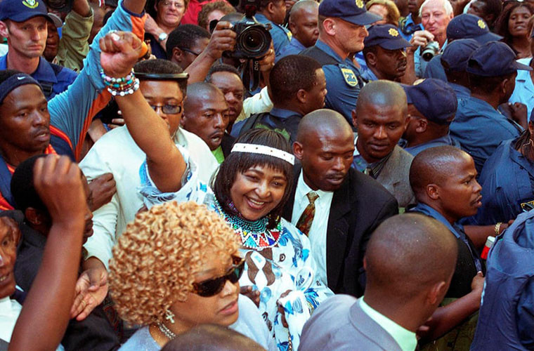 Winnie Mandela giơ tay khi rời khỏi tòa án. Bà dính vào bê bối pháp lý với 43 cáo buộc lừa đảo và 25 cáo buộc trộm cắp tài sản công. Ảnh: AP.