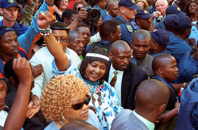 Winnie Mandela giơ tay khi rời khỏi tòa án. Bà dính vào bê bối pháp lý với 43 cáo buộc lừa đảo và 25 cáo buộc trộm cắp tài sản công. Ảnh: AP.