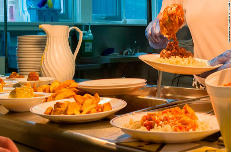 Một người phụ nữ chuẩn bị đồ ăn cho học sinh tại căng tin của trường ở xứ Wales. Thực đơn của bữa ăn bao gồm khoai tây, pizza,...