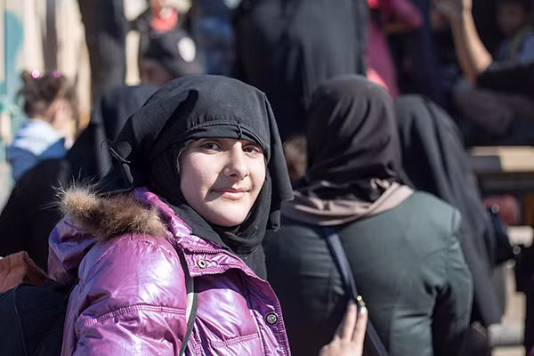 Một cô gái vén mạng che mặt lên và mỉm cười trong lúc chờ được lên xe tải. Được biết, trong thời gian chiếm đóng, phiến quân IS đã bắt phụ nữ phải che mặt ở những nơi công cộng.