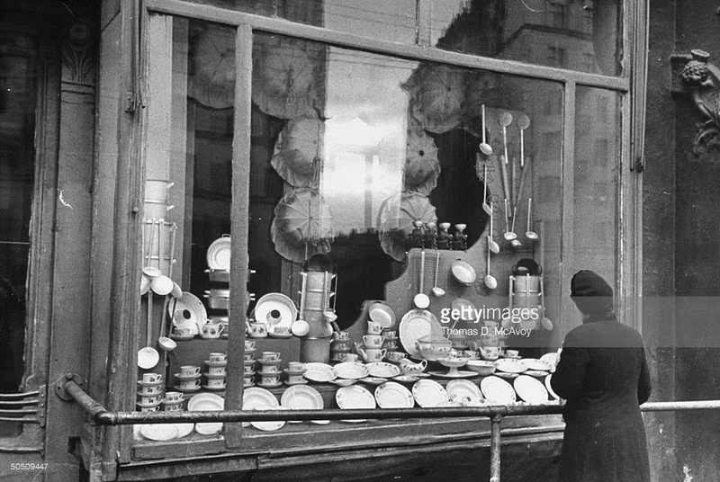 Người phụ nữ đứng trước một quầy hàng đồ dùng nhà bếp, đồ dùng nấu ăn...