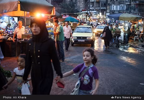 Người phụ nữ dắt hai con nhỏ đi qua khu chợ ở Aleppo.