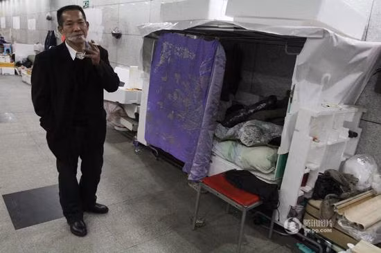 Một người đàn ông vô gia cư hút thuốc cạnh “túp lều” tạm bợ được dựng ngay trong hầm đi bộ. Ảnh: Sina.