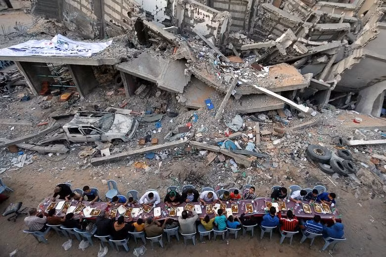 Trong tháng lễ Ramadan, một nhóm người dân Palestine tập trung ăn uống cạnh đống đổ nát của tòa nhà bị phá hủy sau các đợt không kích của Israel tại Dải Gaza.