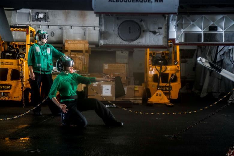 Thuỷ thủ trên tàu sân bay USS Abraham Lincoln xi-nhan cho máy bay F/A-18 được kéo lên thang nâng để đưa lên sàn tàu, sẵn sàng cất cánh. Nguồn ảnh: Reuters.