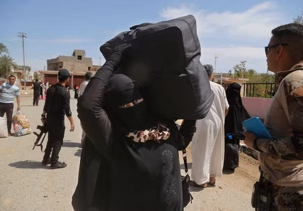 Một phụ nữ Iraq trong bộ trang phục màu đen vác túi đồ đi trên đường phố Heet.