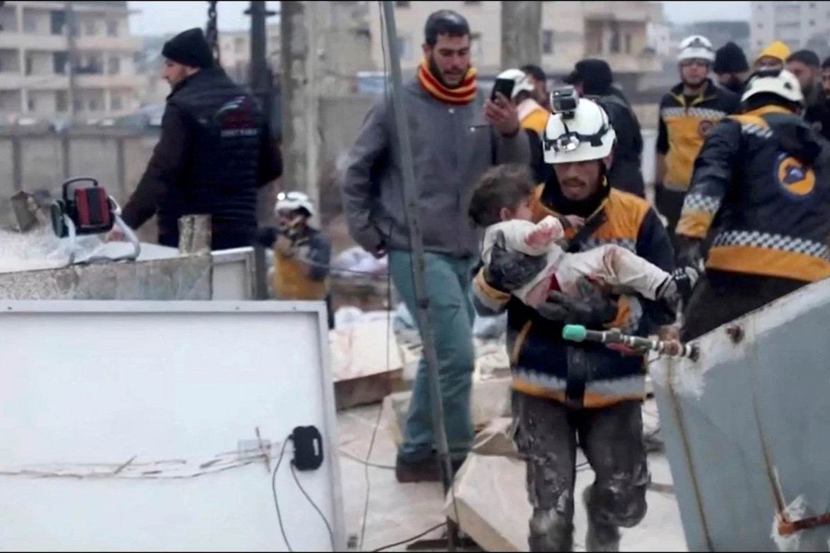 Một nhân viên cứu hộ bế đứa trẻ bị thương ra khỏi đống đổ nát ở Syria. Ảnh: Reuters.