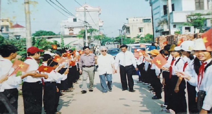 Hình ảnh các cháu học sinh đứng hai bên, cầm cờ vỗ tay vui mừng khi nguyên Tổng Bí thư Đỗ Mười về xã Đông Mỹ dự "Lễ kỷ niệm 80 năm thành lập Chi bộ Đông Phù" năm 2010.
