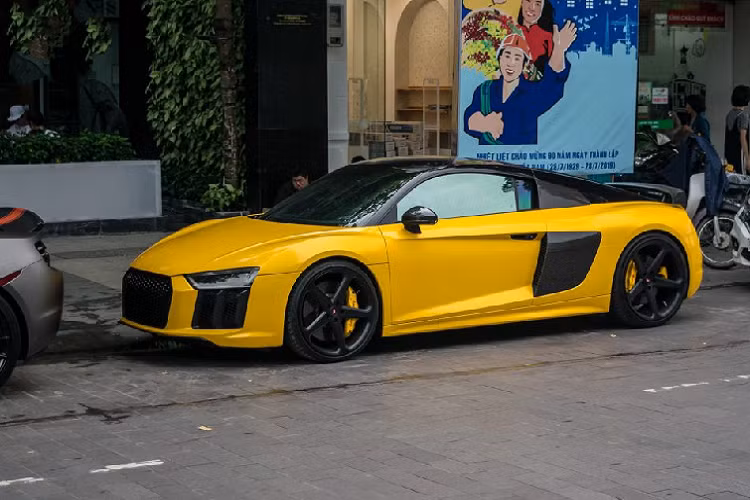 Khác với những lần trước đó, lần này là sự xuất hiện của siêu xe Audi R8 V10 Plus mang màu vàng đậm phối với mui đen. Đây chính là một trong hai chiếc Audi R8 V10 tại Việt Nam mang màu đen nguyên bản, tuy nhiên chiếc xe này gây chú ý hơn khi từng qua tay Cường Đô la.