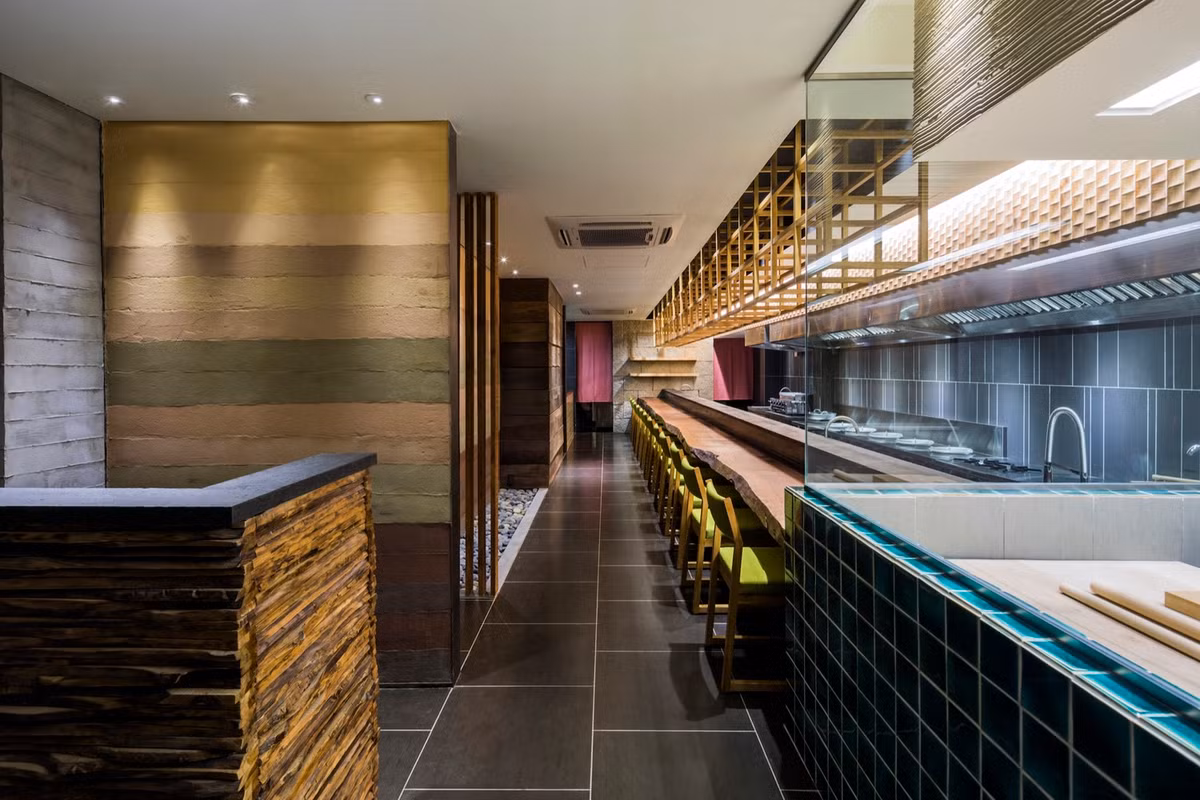 Những chiếc ghế xanh nổi bật trên nền tường màu tối và bàn gỗ dài.