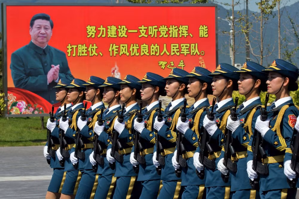 Nữ quân nhân Trung Quốc diễu hành gần tấm bảng có khẩu hiệu "Phấn đấu xây dựng quân đội nhân dân tuân theo đảng, chiến thắng và làm việc xuất sắc.