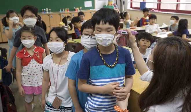 Học sinh một trường tiểu học đeo khẩu trang kín mít trước khi các nhân viên y tế kiểm tra nhiệt độ cơ thể cho các em.