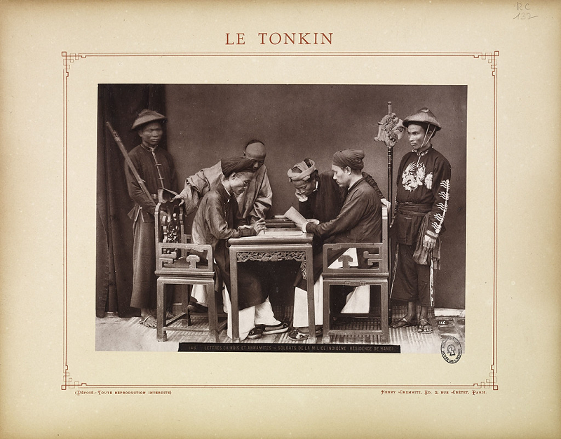 Ảnh hai ông quan xem xét các văn thư, xung quanh là vài thường dân và binh lính.