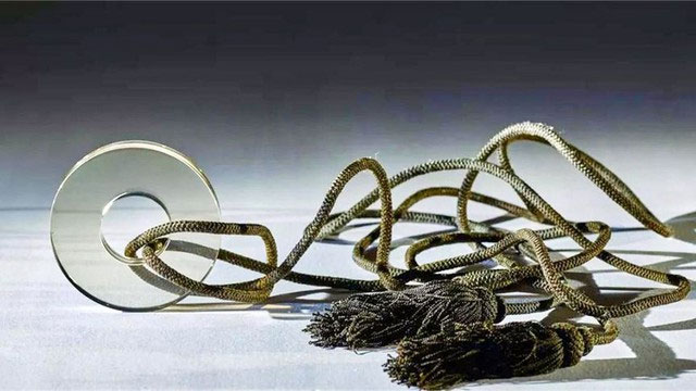 Trong quá trình làm việc xung quanh ngôi mộ cổ được cho là thuộc thời Nam Tống, cách đây 800 năm, chuyên gia phát hiện một vật thể phát sáng khi được ánh sáng chiếu vào, đó là một miếng thủy tinh hình tròn xỏ qua dây. Miếng thủy tinh này khiến các nhà khảo cổ bối rối vì tính hiện đại của nó. (Ảnh: Sohu)