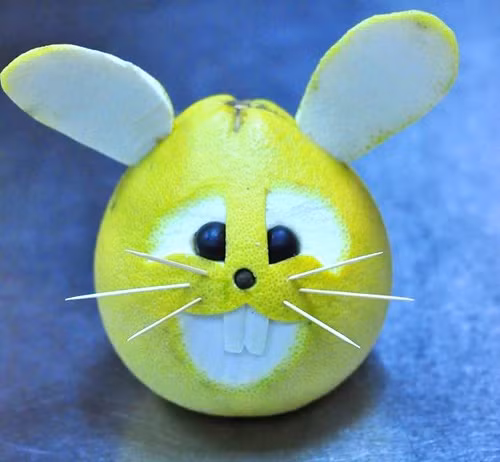 Làm chú thỏ bằng bưởi: Vẽ hình mắt và miệng của chú thỏ lên vỏ bưởi. Sau đó dùng dao tỉa theo hình mà đã vẽ. Tỉa bỏ lớp vỏ xanh hoặc vàng bên ngoài quả bưởi để lộ ra lớp cùi trắng là được. Ở phần miệng của chú thỏ, tỉa một hình chữ nhật nổi lên trên rồi khoét một đường ở giữa tạo thành hai chiếc răng cửa đáng yêu của chú thỏ. Dùng phần vỏ bưởi vừa cắt ra để làm tai thỏ. Gắn hai hạt nhãn vào mắt vào 6 chiếc tăm nhọn làm râu thỏ.