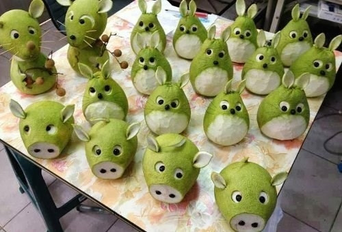 Chú lợn bằng bưởi: Đầu tiên, cắt bỏ phần đầu của quả bưởi. Để quả bưởi nằm ngang rồi ước lượng vị trí cân đối của hai con mắt, khoét phần vỏ xanh đi, để lộ phần cùi trắng. Dùng phần vỏ vừa cắt bỏ để làm tai heo. Sau đó, bạn gắn hạt nhãn vào vị trí hai lỗ mũi và mắt của chú heo.