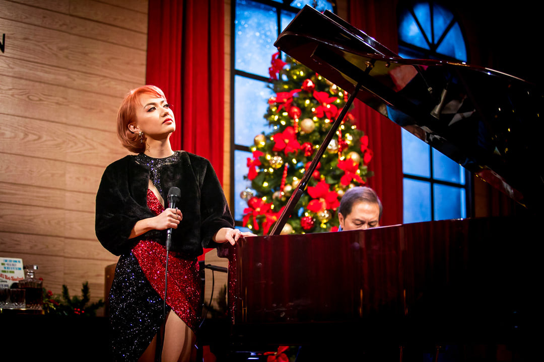 Xuân Nghi diện đồ đông màu trắng đỏ hát trong buổi lễ gần Giáng Sinh.