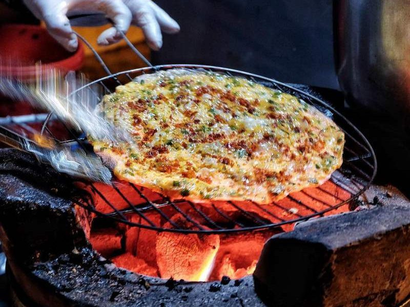 Bánh tráng nướng tại đây có 3 hương vị chính là phô mai, pate, mayonnaise, được nướng kèm cùng các nguyên liệu chà bông, xúc xích, mỡ hành... ăn khá ngon. Tuy nhiên quán ăn "chửi khách" này nằm ngoài lề đường, thường rất đông khách nên sẽ không thích hợp đi nhóm đông người. Ảnh: Internet.