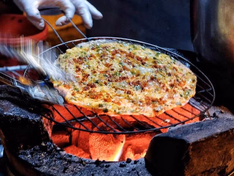 Bánh tráng nướng tại đây có 3 hương vị chính là phô mai, pate, mayonnaise, được nướng kèm cùng các nguyên liệu chà bông, xúc xích, mỡ hành... ăn khá ngon. Tuy nhiên quán ăn "chửi khách" này nằm ngoài lề đường, thường rất đông khách nên sẽ không thích hợp đi nhóm đông người. Ảnh: Internet.