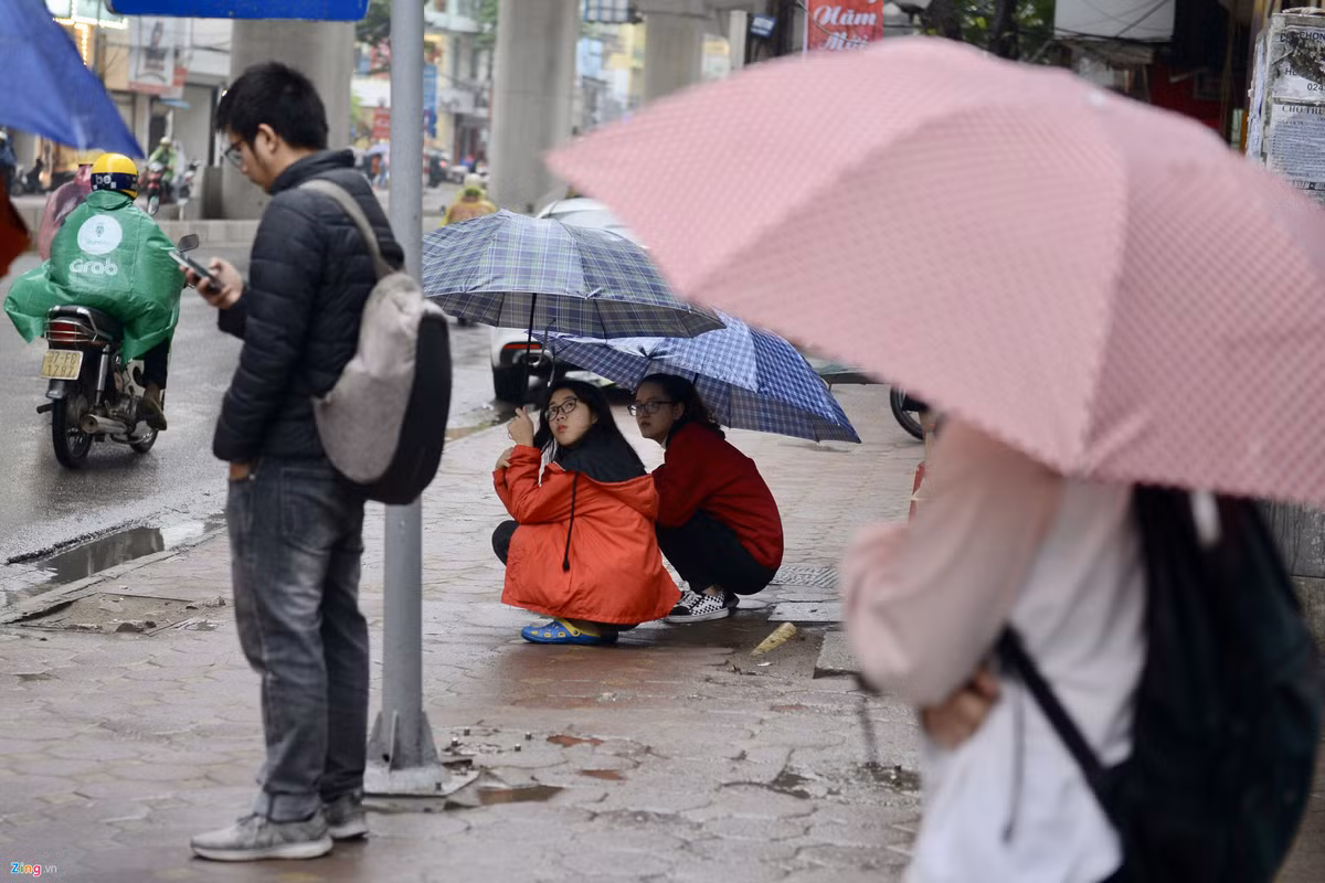 Hai em học sinh ngồi co ro trong khi chờ xe buýt trên đường Cầu Giấy.