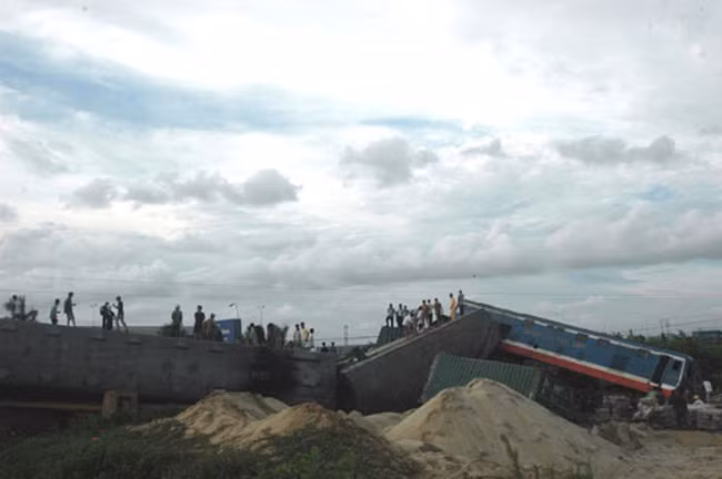 Đoạn đường sắt nơi xảy ra tai nạn bị hư hại nặng, 3 toa tàu nằm đổ ngổn ngang. Cạnh đó, xe container bị tàu đâm biến dạng hoàn toàn. Nguồn ảnh: CAND.