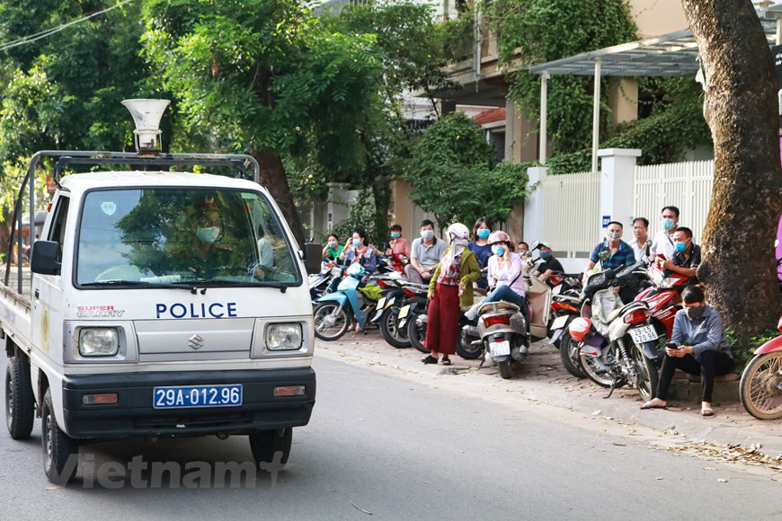 Không chỉ thí sinh, phụ huynh đợi bên ngoài cổng trường cũng được yêu cầu thực hiện nghiêm chỉnh công tác phòng chống dịch. Mọi người liên tục được lực lượng cảnh sát nhắc nhở đeo khẩu trang và đứng giãn cách. (Ảnh: Nguyên An/Vietnam+)