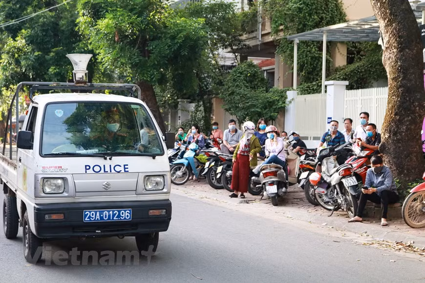 Không chỉ thí sinh, phụ huynh đợi bên ngoài cổng trường cũng được yêu cầu thực hiện nghiêm chỉnh công tác phòng chống dịch. Mọi người liên tục được lực lượng cảnh sát nhắc nhở đeo khẩu trang và đứng giãn cách. (Ảnh: Nguyên An/Vietnam+)